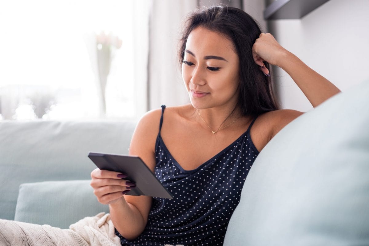 young,asian,woman,sitting,on,sofa,using,reader,tablet,and