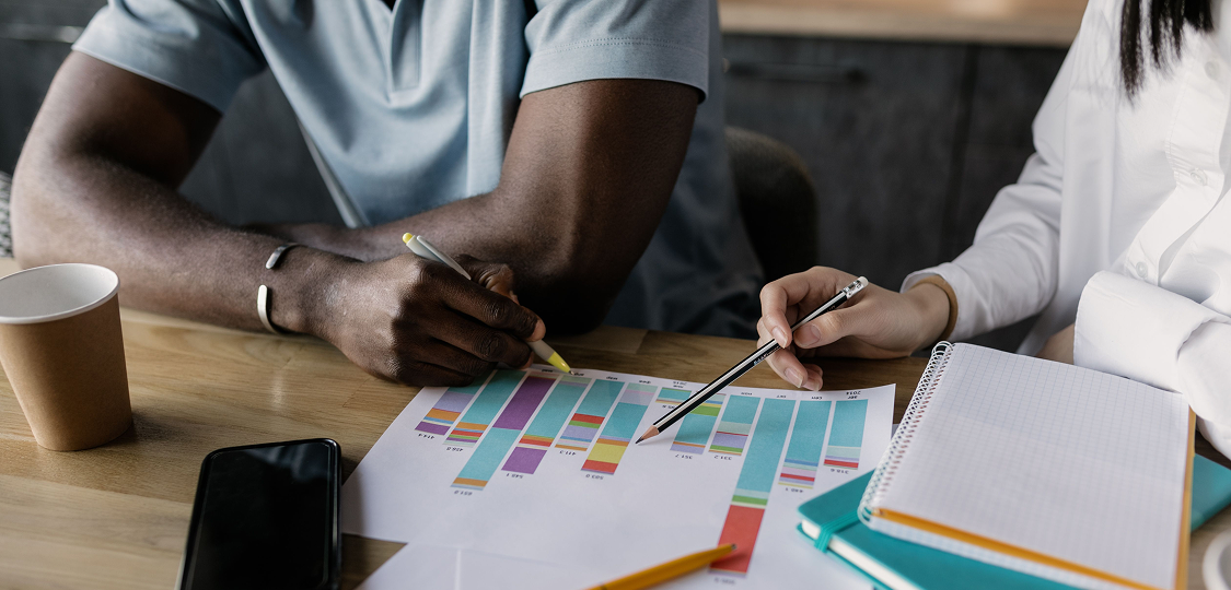 Two colleagues reviewing a printed bar chart with pencils at a desk, discussing AI readiness assessment results