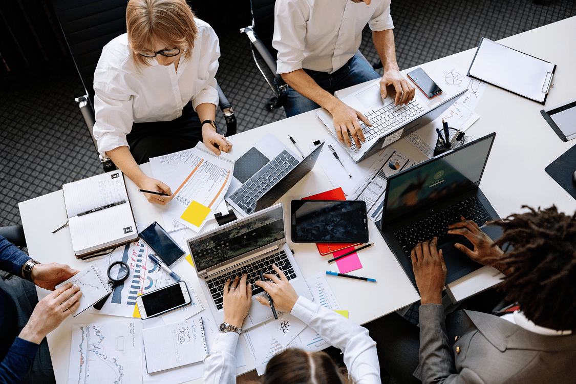 Team of employees collaborating around a table with laptops during an AI rollout